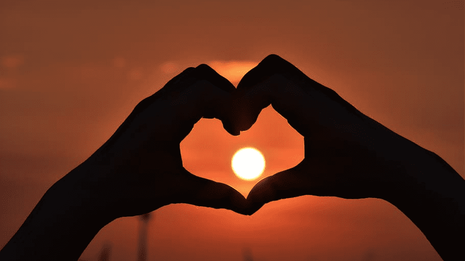 a silhouette of hands making a heart shape with the sun in the background