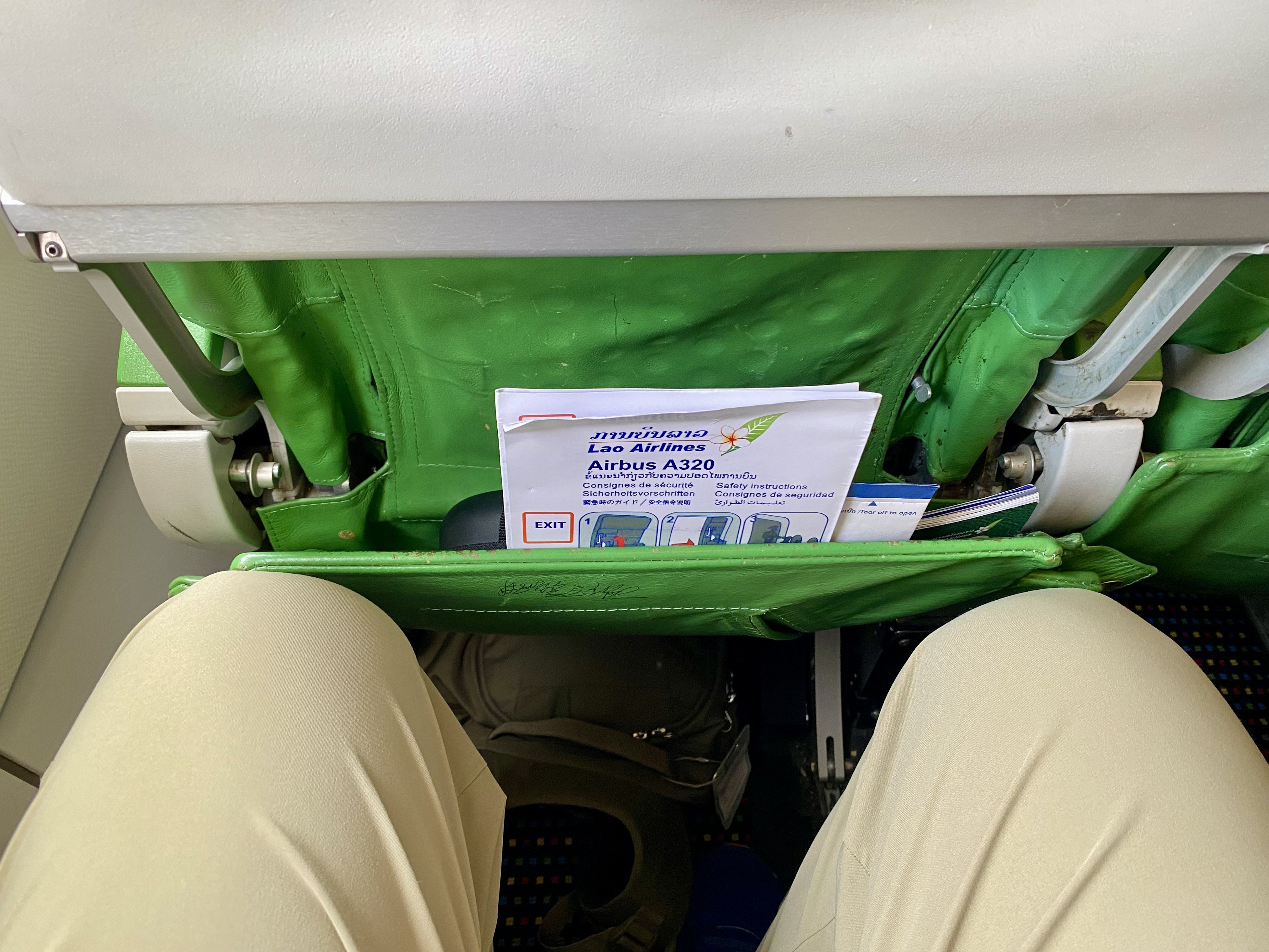 a person's legs in a green seat with a paper in it