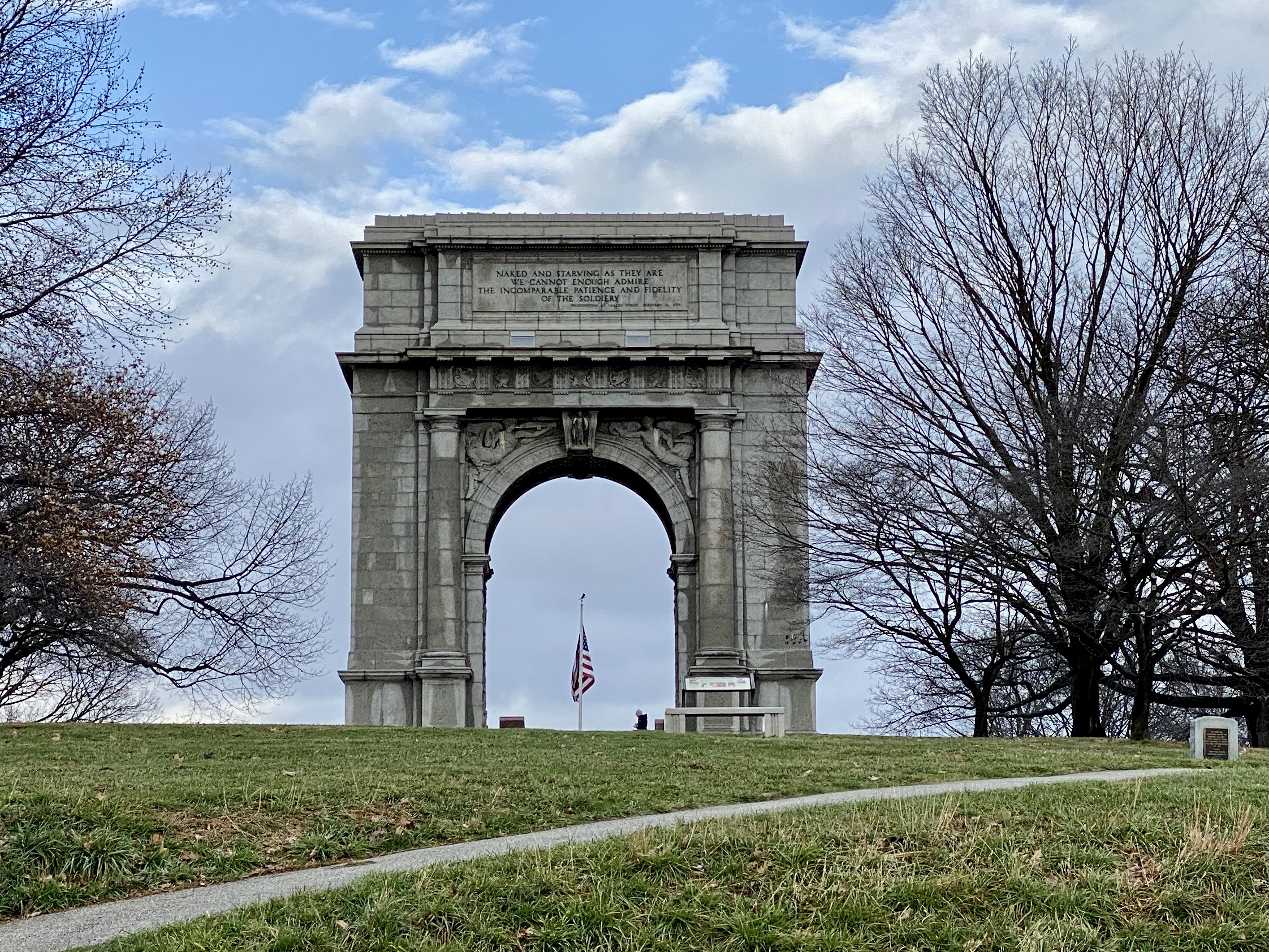 a stone arch with a flag on the top of it with Arch of Triumph in the background