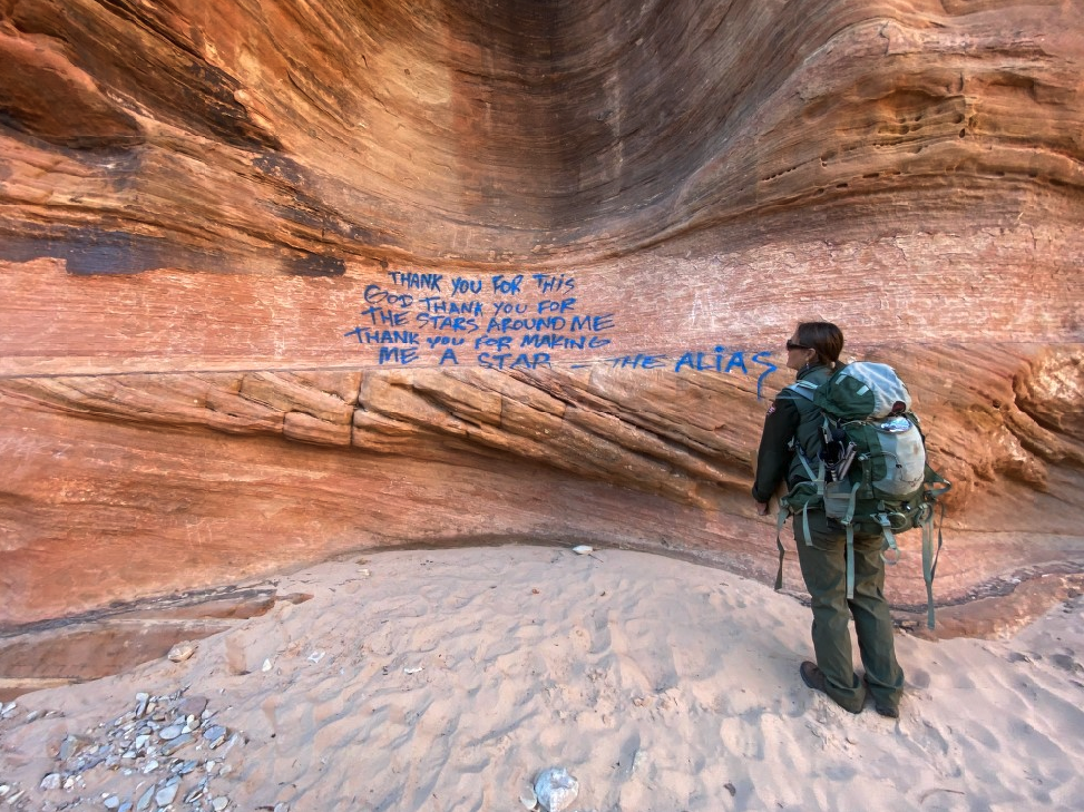 a person standing in front of a rock wall with blue writing