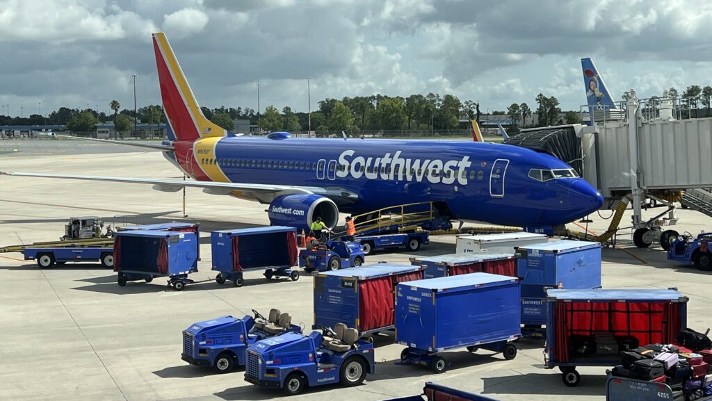 a blue airplane with luggage carts and people on it