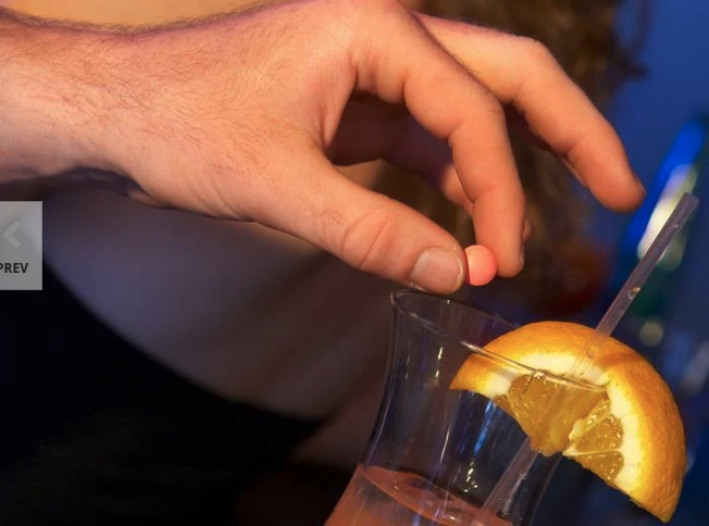 a hand holding a pill to a glass of liquid