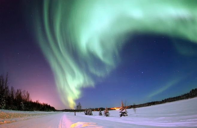 a green and purple aurora borealis in the sky over a snowy field