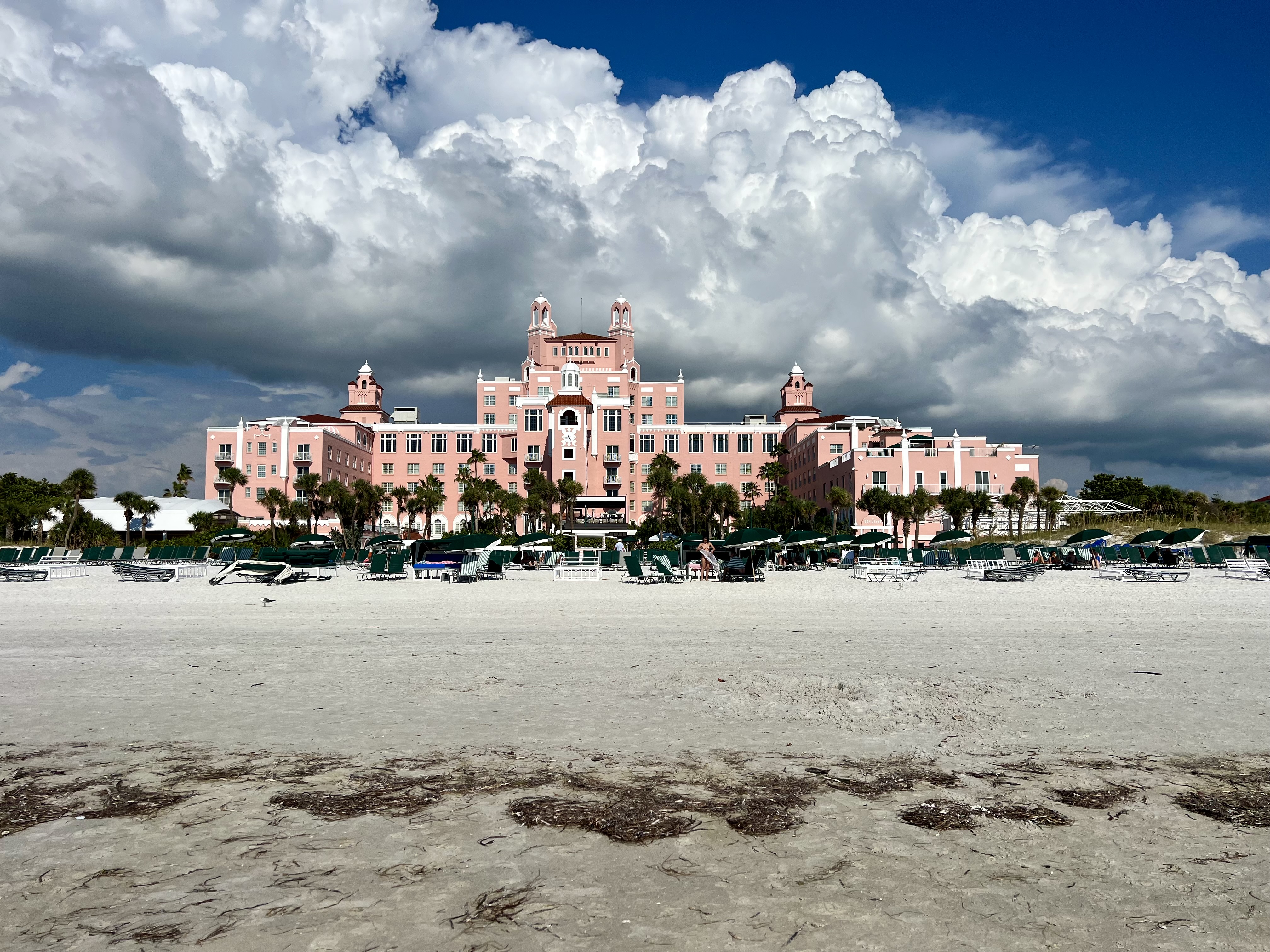 a large pink building with trees and a beach in the background with Don CeSar in the background