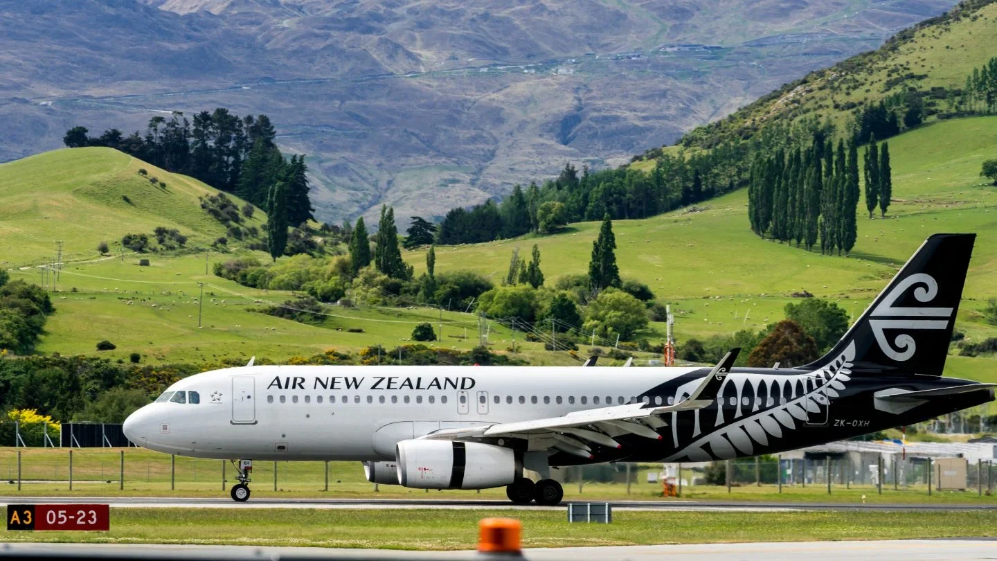 a white airplane on a runway with trees and mountains in the background