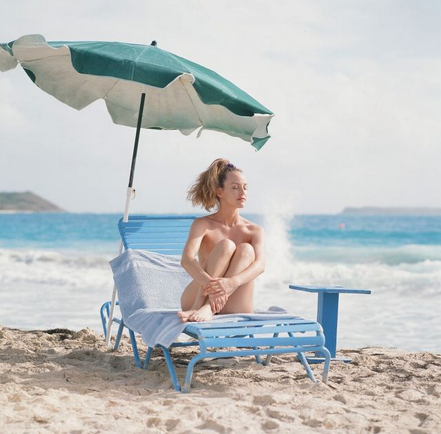 a woman sitting on a beach chair under an umbrella