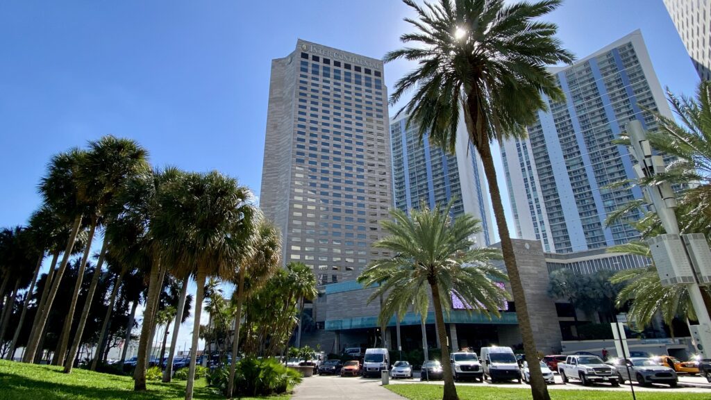 a tall building with palm trees and a parking lot