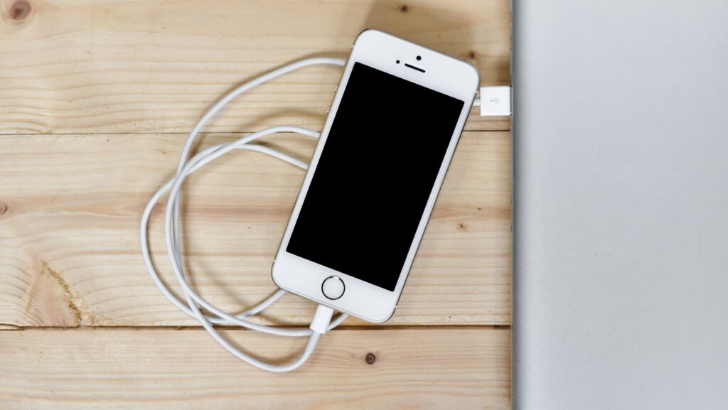 a white cell phone with a white cable plugged into a laptop