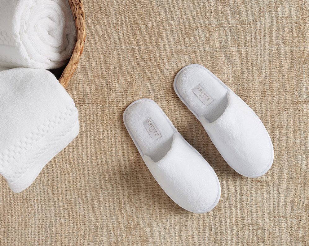 a pair of white slippers next to a basket of towels