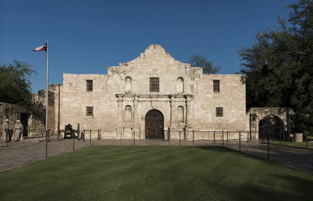 a stone building with a green lawn with Alamo Mission in San Antonio in the background