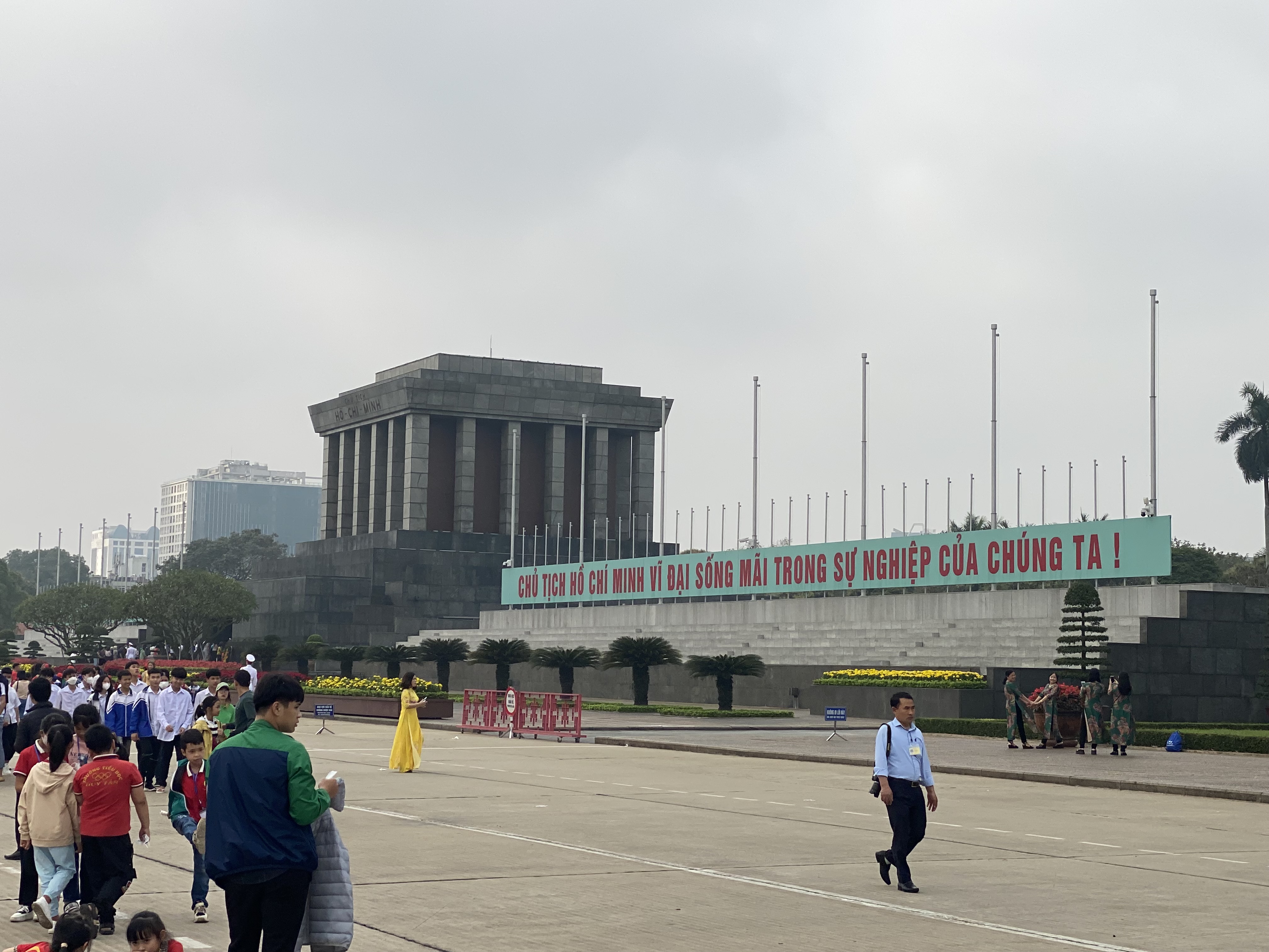 a group of people walking on a road with Ho Chi Minh Mausoleum in the background