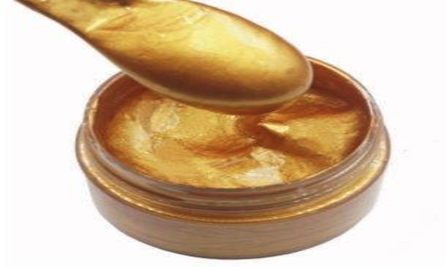 a spoon over a jar of gold paint