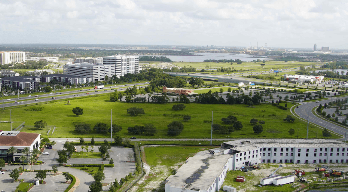 a green field with buildings and a body of water