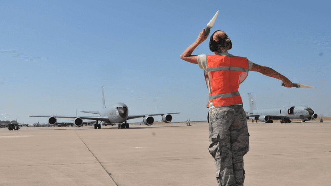 a woman in military uniform standing on a runway with a plane in the background