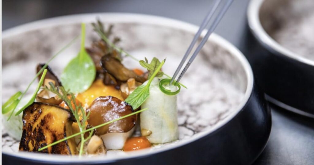 Close-up of a fine dining dish at Victoria & Albert’s, featuring artistically plated vegetables and garnishes being arranged with precision tweezers.