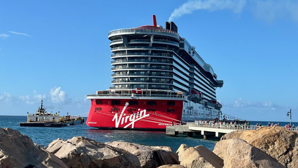 a large cruise ship docked in the water with West Quoddy Head Light in the background