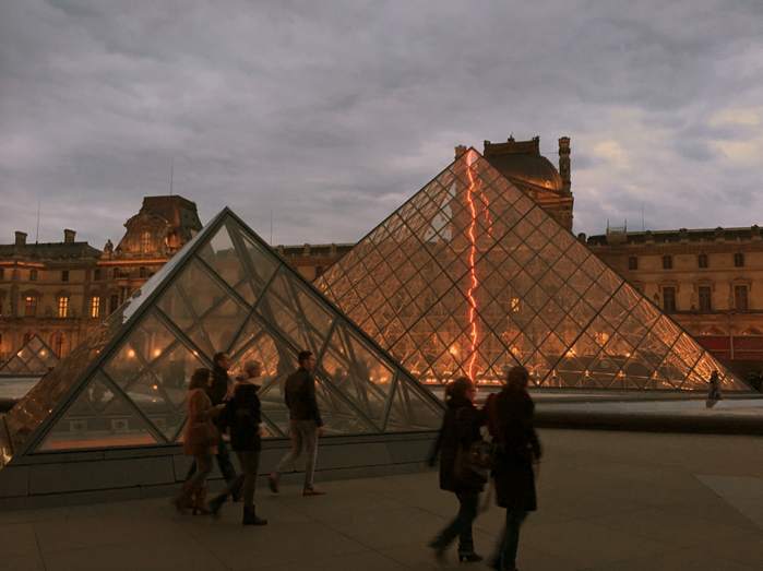 a group of people walking by a glass pyramid