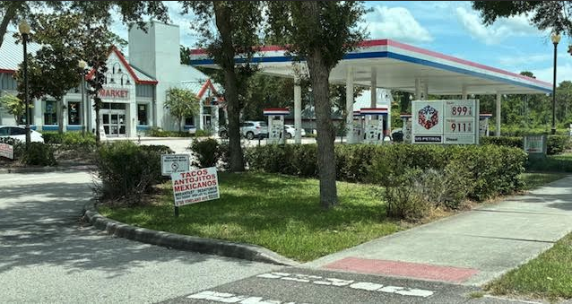 a gas station with a sign and a tree