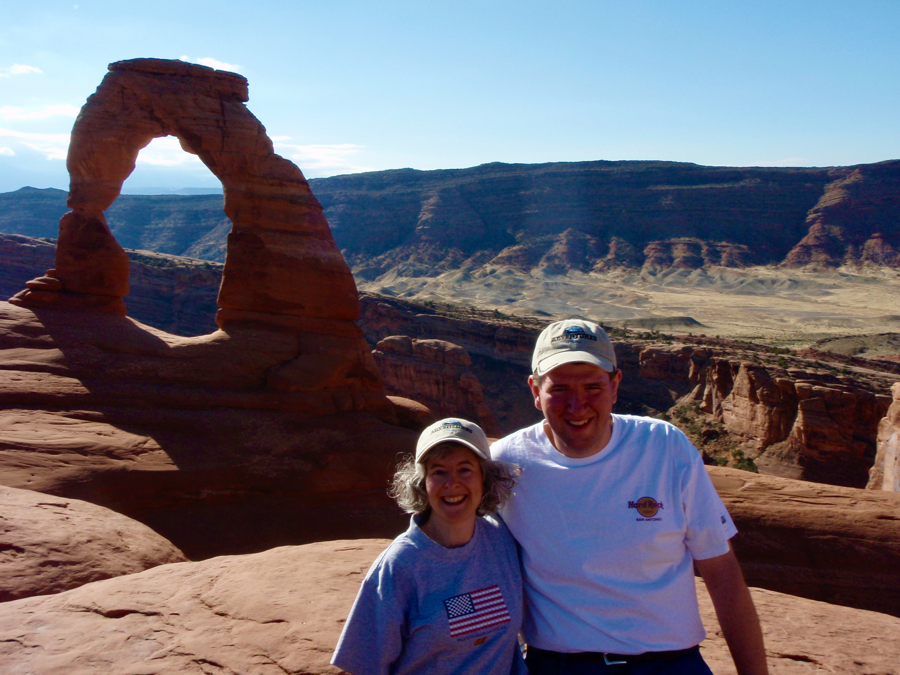 Visitors posing near Delicate Arch with desert landscape behind them