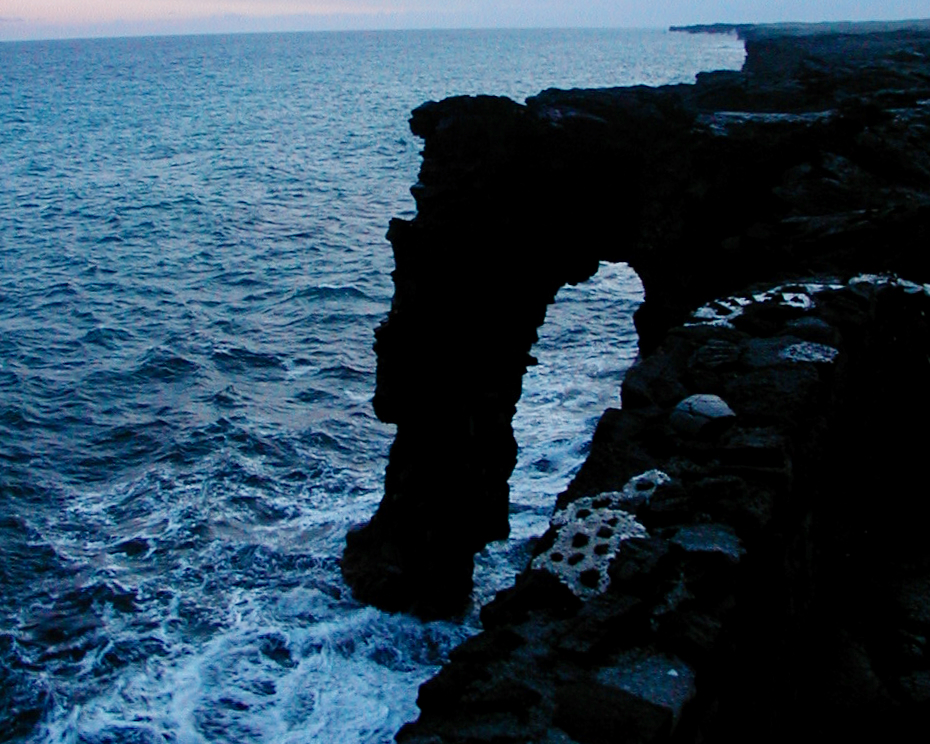 A natural lava sea arch on a rocky coastline with ocean waves below